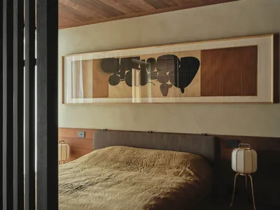 A minimalist bedroom featuring a wooden bed frame and headboard, with a large framed abstract painting above it.