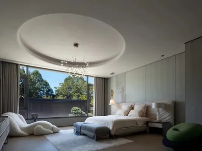 Modern bedroom with neutral-toned decor and large windows overlooking greenery.