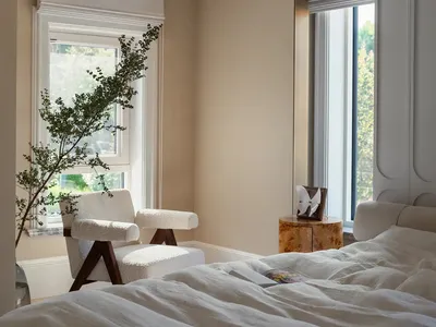 A modern minimalist bedroom with white textiles, featuring a large bed with a canopy and a white armchair.