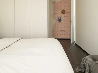 A minimalist bedroom featuring a white bed with a modern design, surrounded by white closet doors and a pink pegboard wall fe