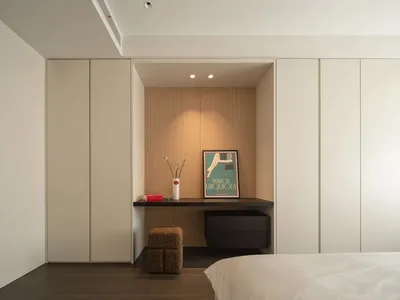 A minimalist bedroom with a bed, white bedding, a wooden desk, and a poster on the wall.