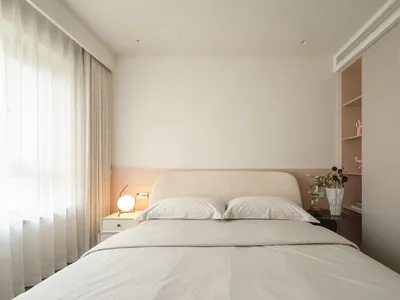 A minimalist bedroom with a neutral color palette, white bed, and simple furnishings.