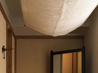 A minimalist bedroom with wooden floors, a candle holder with two lit candles, and a large mirror reflecting a door.