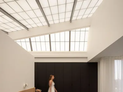 The image showcases a modern minimalist bedroom featuring neutral tones and a high ceiling with skylights.