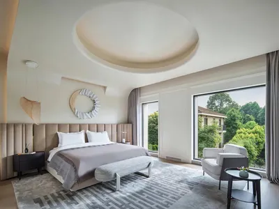 A modern, minimalist bedroom with a large bed, window, and white decor.
