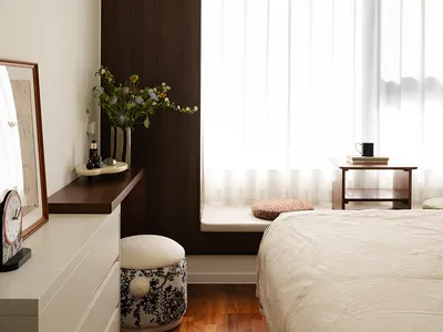 Minimalist bedroom interior with white wood furniture, a large window with sheer curtains, and a bed with a textured blanket.