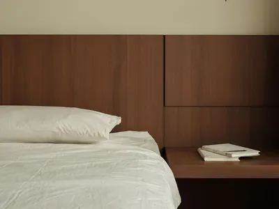Modern, minimalist bedroom featuring wooden headboard and floating nightstand with books.