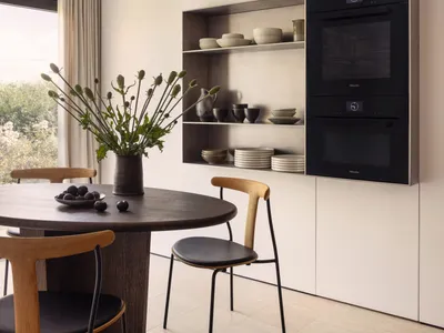 Modern kitchen featuring wooden table and chairs with stainless steel appliances and open shelving.