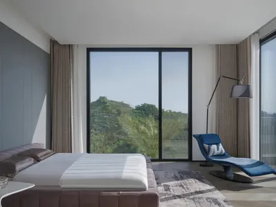 A modern minimalist bedroom featuring a sleek, upholstered bed with a glass headboard, a smart touch bedside table, and a con