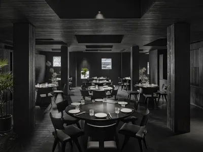 Circular tables and chairs in a minimalist restaurant interior with dark wooden flooring and ceiling.