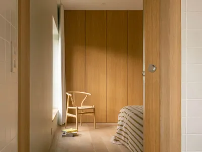 A minimalist bedroom with wooden floors, a single chair, and a bed with striped sheets.