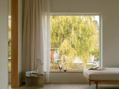 A minimalist bedroom featuring a wood floor, a daybed, and a window with a view of autumn trees.