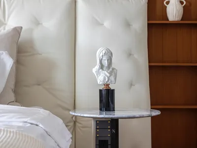 A minimalist bedroom featuring a leather headboard with tufted cushions, a marble bedside table, and a wooden bookshelf with