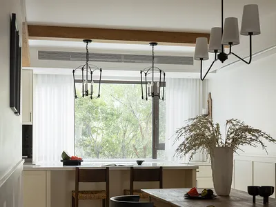 Modern country-style kitchen with wooden furniture and fabric accents, featuring a large window and chandelier lighting.