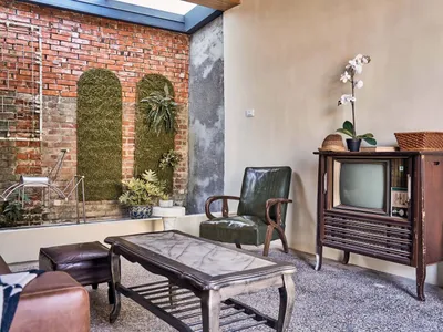 An industrial-style living room with brick walls, leather furniture, glass table, and wooden TV cabinet.