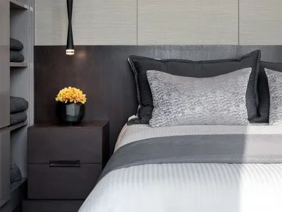 Minimalist bedroom with a bed adorned with gray and black pillows, a white bedspread, and a wooden headboard with metallic el