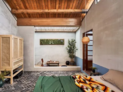 A modern bedroom with a concrete wall, wooden ceiling, and a cozy seating area.