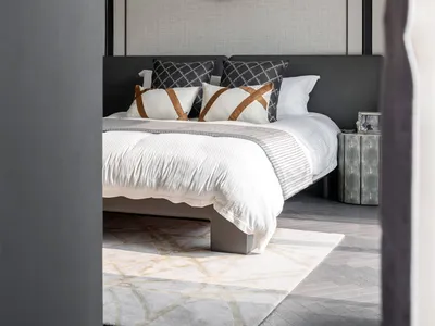 Modern bedroom featuring a bed with a fabric headboard, metallic nightstand, and abstract wall art.