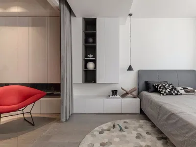 A modern bedroom featuring a concrete floor and minimalist decor with a gray bed and white cabinets.