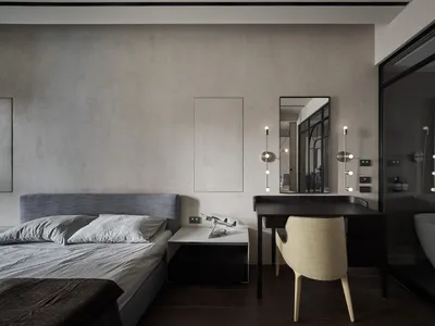 Minimalist bedroom with neutral tones and black furniture, featuring a bed, a desk, and a bathroom in the background.