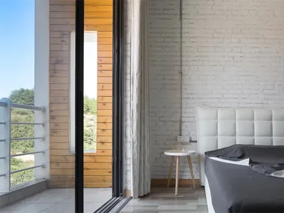 A minimalist bedroom featuring a white brick wall, wooden flooring, and a bed with a grey cover.
