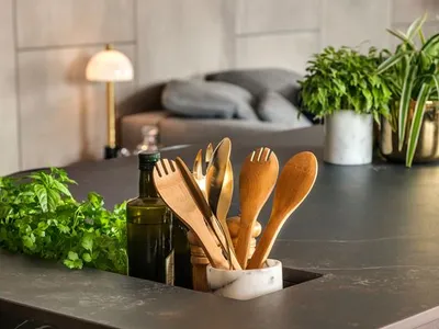 A modern kitchen with stone countertops, wooden utensils, and green plants on the countertop.