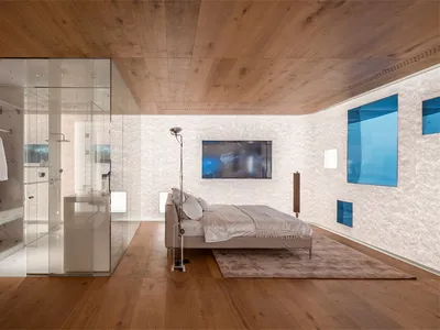 A minimalist bedroom featuring wooden furniture and a glass-enclosed shower area.
