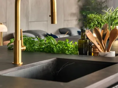 Modern minimalist kitchen with a sleek, curved gold faucet and greenery on the countertop.