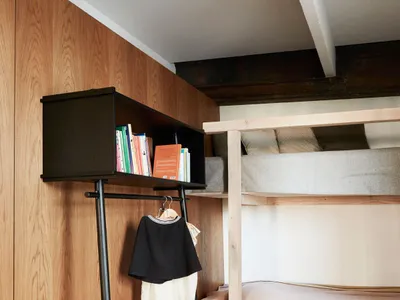 A minimalist bedroom with wooden walls and furniture, featuring a bunk bed and a black freestanding wardrobe.