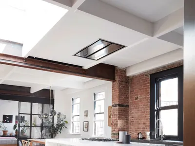 A modern kitchen featuring a white marble island, glass pendant lights, and an exposed brick wall.