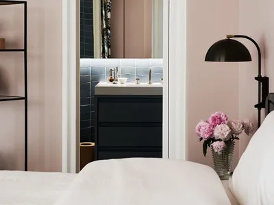 A minimalist bedroom with a pink wall, white furniture, and a mirror.