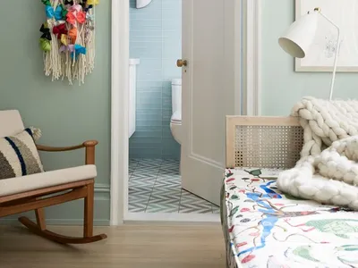 A bedroom with a wooden bed, colorful fabric, and yarn decoration against a pastel green wall.