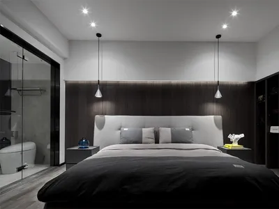 Minimalist bedroom with a large bed, gray headboard, and black and gray bedding. Modern lighting fixtures and a bathroom area