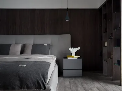 A modern minimalist bedroom featuring wood-paneled walls, a grey upholstered bed, and a grey wooden nightstand with books and