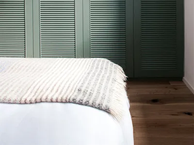 Minimalist bedroom with wooden flooring and a partially visible bed with a white and beige striped blanket.