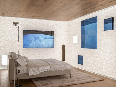 A minimalist bedroom featuring wooden flooring, walls, and ceiling, with a bed, television, and lamp.