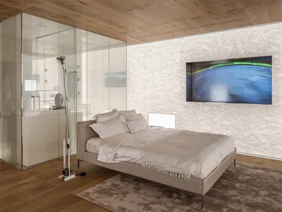 Minimalist bedroom with a glass shower enclosure, wooden floor, and a bed with white bedding.