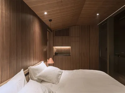 A minimalist bedroom with a bed, white bedding, and wood walls and ceiling.