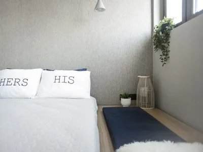 一間簡約臥室，設有特大雙人床，配有「Hers」與「His」枕頭、藍色抱枕，以及一扇可見綠意的窗戶