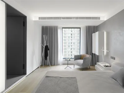 A modern bedroom with a minimalist design, featuring a bed, armchair, and window with curtains, all in neutral tones.