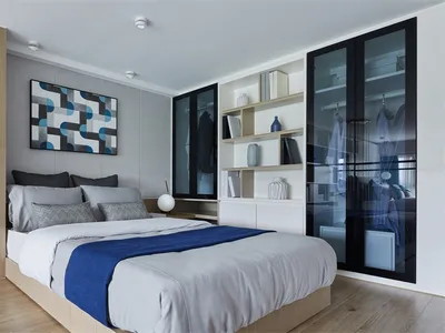 Modern bedroom with white walls and bed, featuring a blue and white geometric artwork on the wall.