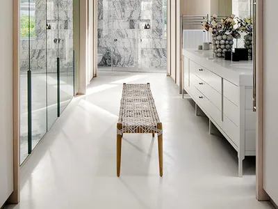 Modern bathroom with white marble walls, white floor, white bench, and white cabinetry with metallic accents.