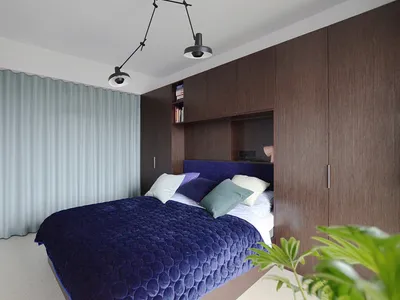 A minimalist bedroom featuring dark wood furniture and a dark blue quilted blanket.