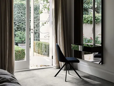 Minimalist bedroom featuring a metallic chair, glass mirror, and fabric curtains.