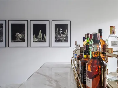 A modern bar area featuring a marble countertop with a selection of liquor bottles and framed artwork on the wall.
