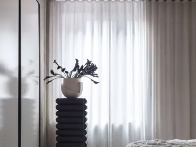 一間極簡臥室，擺放質感沙發與其他質感元素，搭配白色窗簾與混凝土天花板。