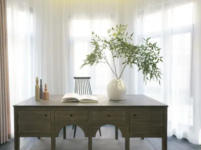 A modern home office setup featuring a wooden desk with a ceramic vase and green plant, and a wooden chair.