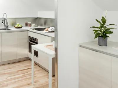 A modern kitchen with a wooden floor, white countertops, and stainless steel appliances.