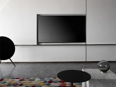 A minimalist living room with a concrete wall, television mounted on it, and a colorful rug on a polished concrete floor.