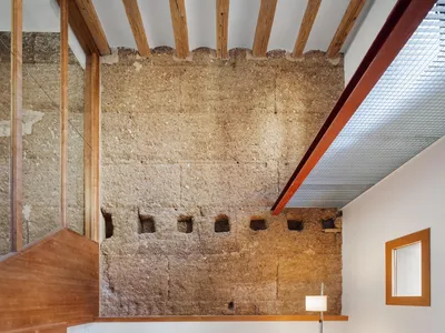 minimalist-style living room with exposed concrete walls and simple wooden furniture, including a chair with a woven backrest